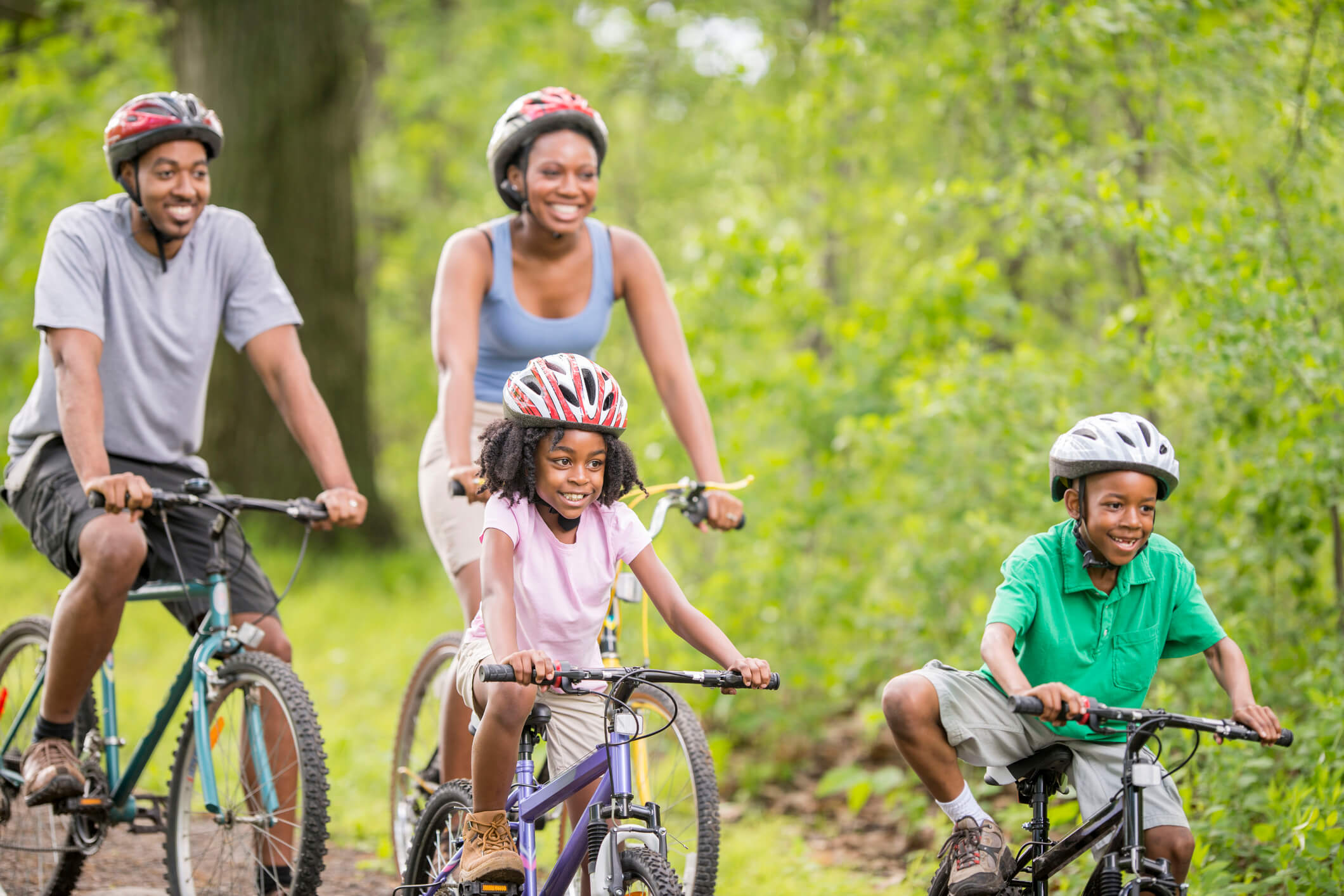 A family is going on a bike ride through the woods while on summer vacation.