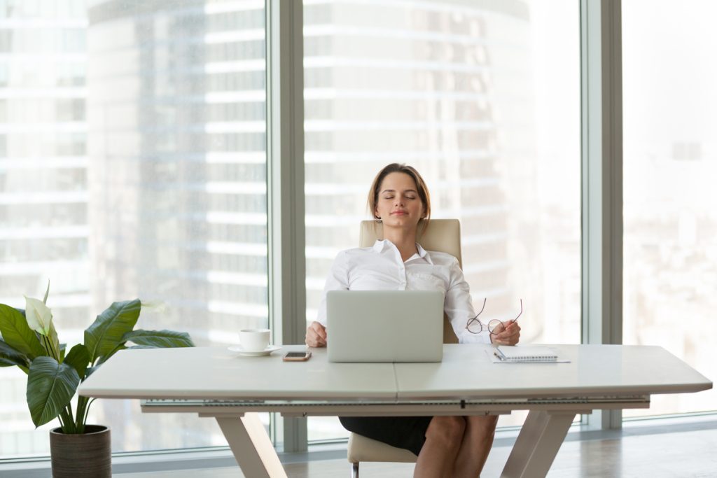 Young businesswoman relaxing leaning on comfortable ergonomic chair in modern office room, calm happy employee feels no stress free relief taking break to rest from computer work breathing fresh air